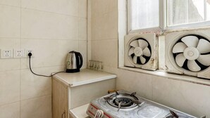A small room with a window, a kettle, a fan, and a stove.