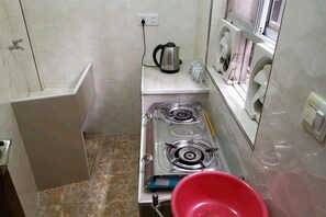 A compact kitchen with a gas stove, a kettle, and a red basin.