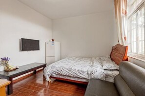 Een slaapkamer met een bed, een bureau, een stoel, een televisie en een raam met gordijnen.