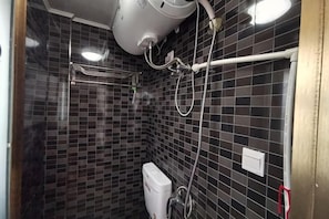 A bathroom with black tiled walls, a white toilet, and a shower area with a handheld showerhead.