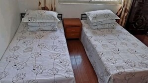 A room with two single beds, each with a floral-patterned bedspread and matching pillows, a wooden nightstand between them, and a window with curtains.