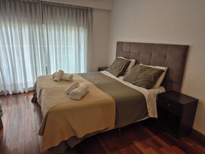 A hotel room with a large bed, a nightstand, and a window with curtains.