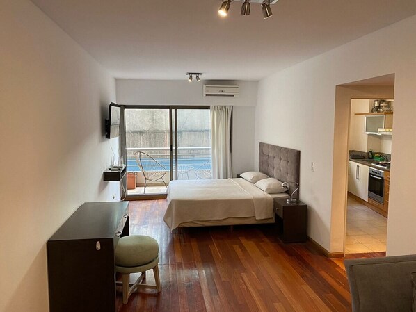 Una habitación de hotel moderna con cama, escritorio, silla, kitchenette y un amplio ventanal con vistas.