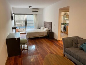 A hotel room with a bed, a desk, a chair, a sofa, and a kitchenette.