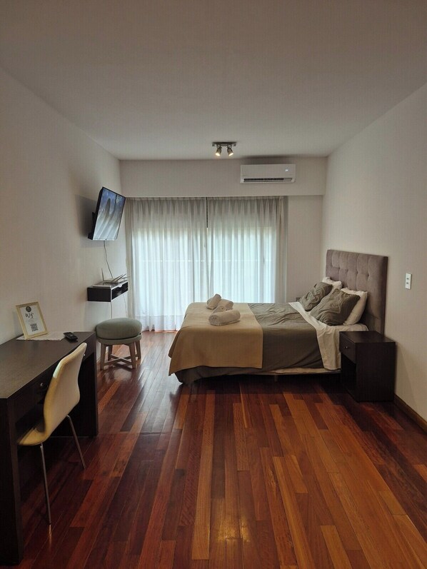 A hotel room with a bed, a desk, a chair, a TV, and a window with curtains.