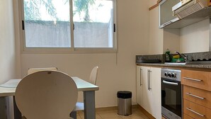 Een keuken met een eettafel, stoelen, een prullenbak en een fornuis.