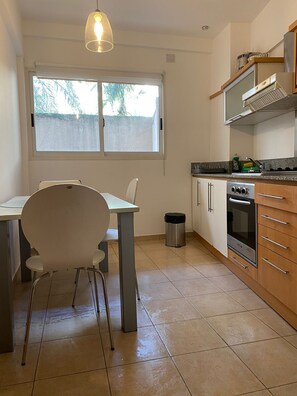 A kitchen with a dining table, chairs, a trash bin, and a stove.