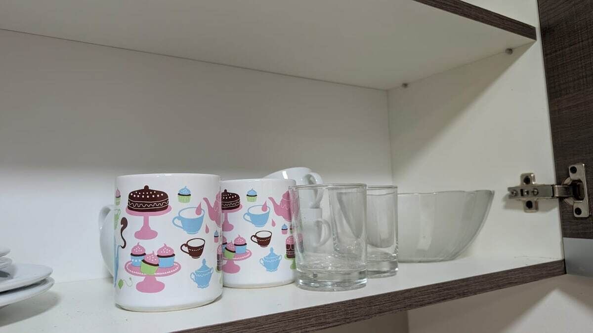 Une étagère de cuisine avec une tasse blanche, un pichet et deux verres transparents.