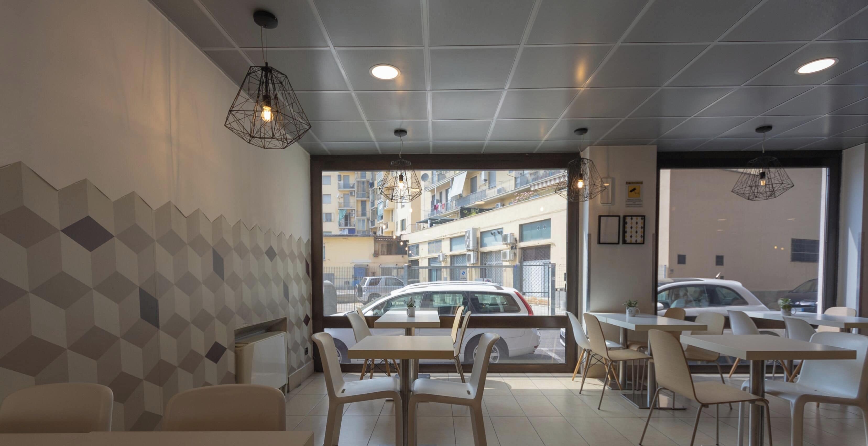 Un interno di un caffè moderno con pareti a motivi geometrici, diverse aree salotto e vista sulla strada.