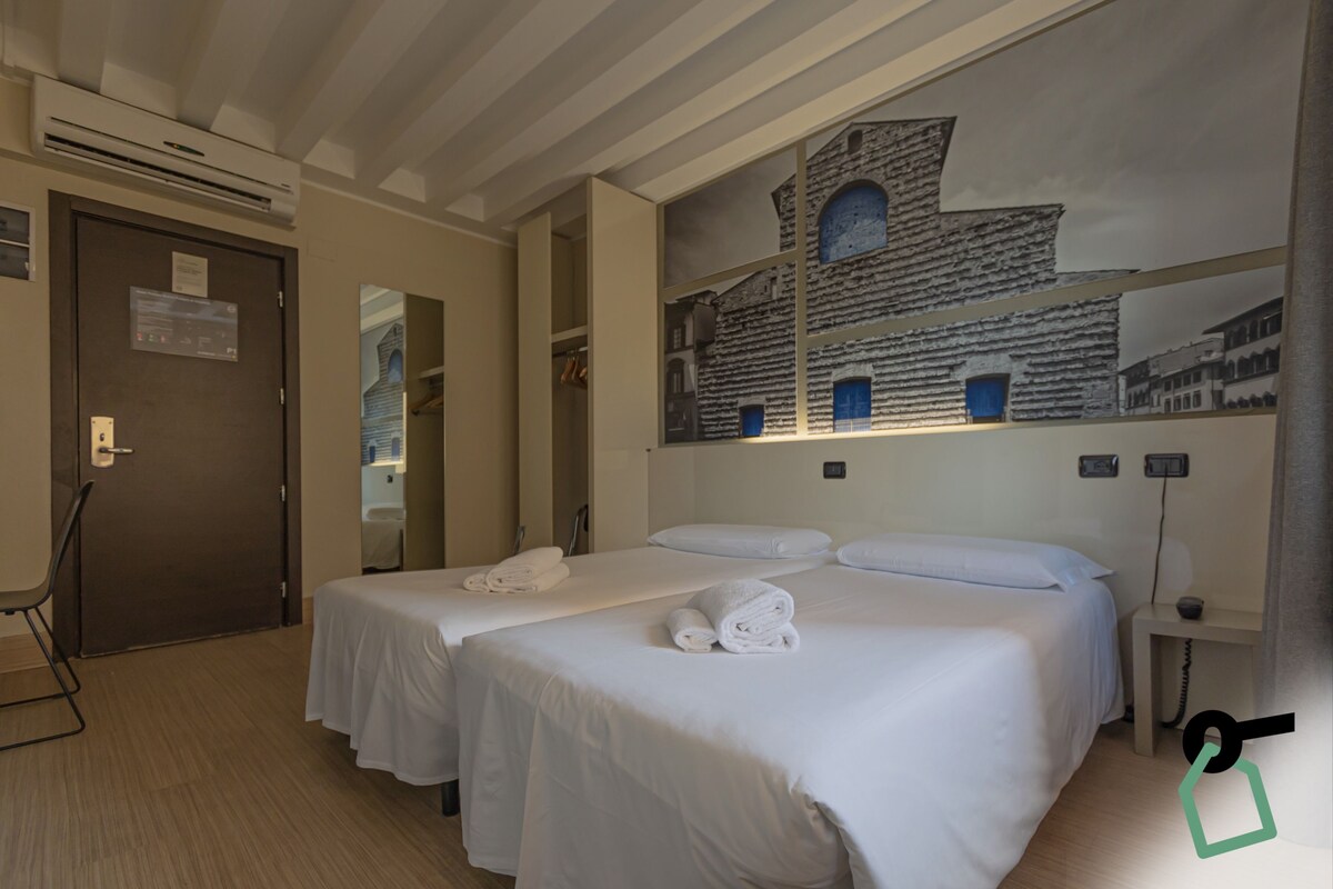 A hotel room with two beds, a large wall mural, a small table, and a chair.