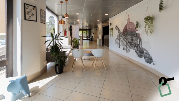 A modern hotel lobby with a long corridor, potted plants, and a mural of a building. - Hotiday Firenze Guidoni (Florence)