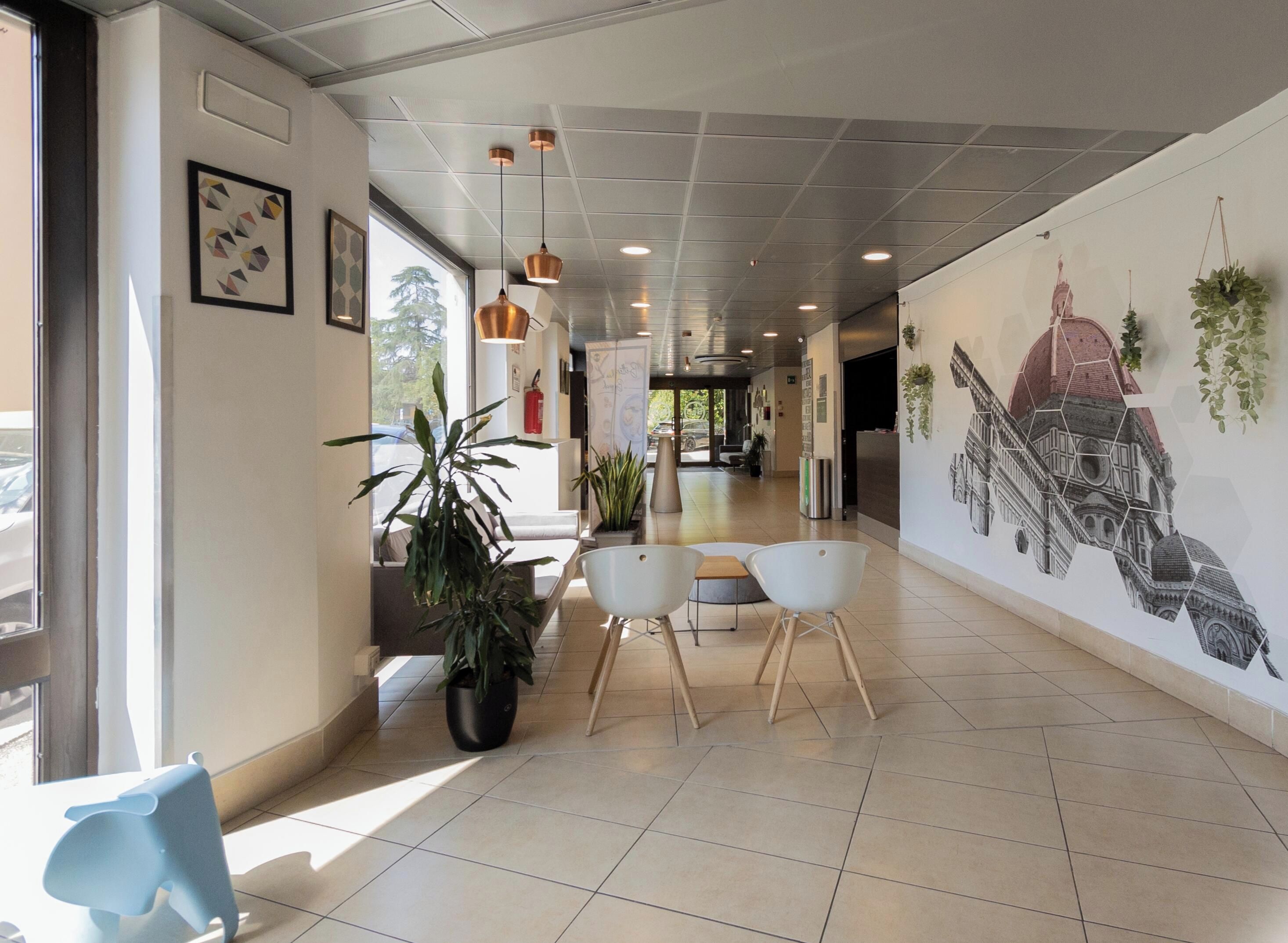A modern hotel lobby with a long corridor, potted plants, and a mural of a building.