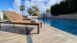 Un espace aménagé au bord de la piscine, avec une chaise longue en bois, une serviette et un mur en pierre.