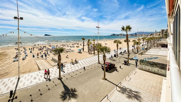A beachside promenade with palm trees, beach umbrellas, and a clear view of the sea.