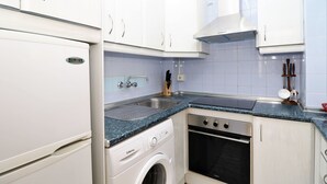 Cocina compacta con armarios blancos, lavadora integrada, lavavajillas y estufa.