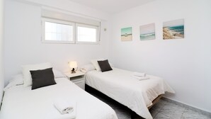Un dormitorio limpio y minimalista con dos camas, una mesita de noche y un ventanal.