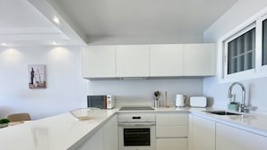 Uma cozinha moderna com armários brancos, forno embutido, micro-ondas e pia com torneira.