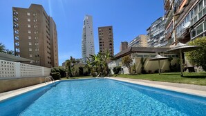 Piscina cercada por edifícios altos, com um céu claro acima.