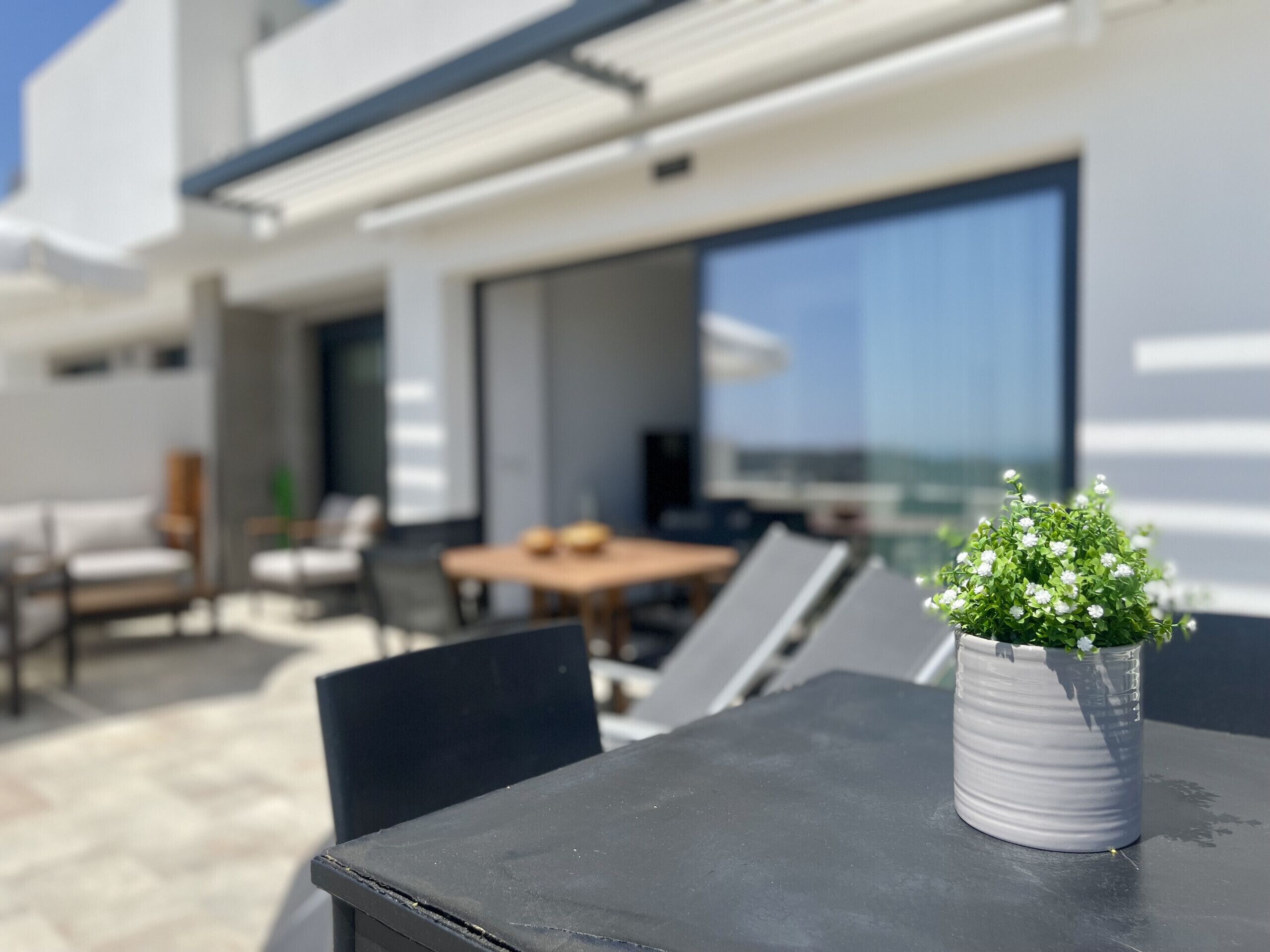 Un área de estar moderna al aire libre con una mesa y sillas, una planta en maceta y vistas a un edificio al fondo.