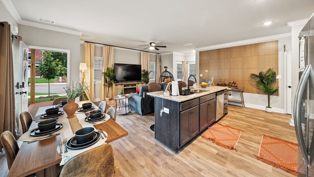 Une cuisine moderne dotée d’un îlot central, d’un coin repas avec une table en bois et d’un espace de vie comprenant un canapé et un téléviseur.