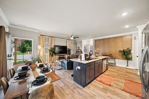 Une cuisine moderne dotée d’un îlot central, d’un coin repas avec une table en bois et d’un espace de vie comprenant un canapé et un téléviseur.