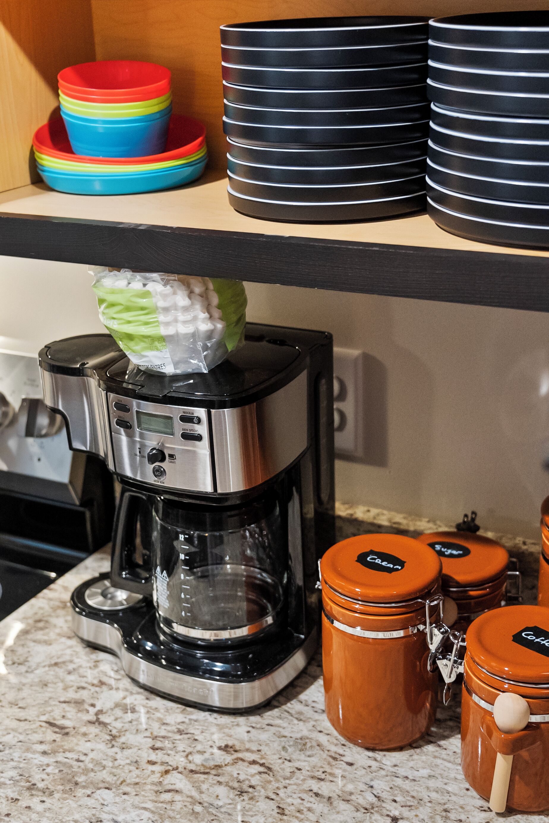 Eine Küche mit einer Kaffeemaschine, gestapelten Tellern und Gläsern auf der Arbeitsfläche.