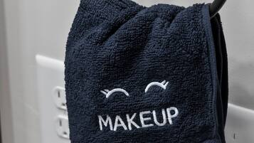 Una toalla azul oscuro con la palabra "MAKEUP" y una carita sonriente colgada de un gancho metálico.