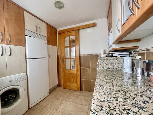 A kitchen with wooden cabinets, a built-in washing machine, a granite countertop, and a coffee maker.