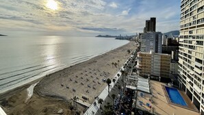 A beachside view with a pool area, beach umbrellas, and a city skyline in the background. - TORRE YAGO SEAFRONT LEVANTE N028 (Benidorm)