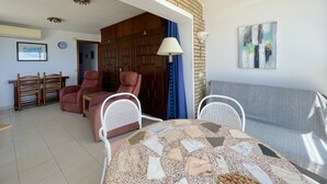 Une pièce comprenant une table à manger, deux chaises, un canapé, une lampe et une porte donnant sur une autre pièce.