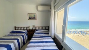 Une chambre avec deux lits, une fenêtre donnant sur la plage, un climatiseur et un tableau au mur.