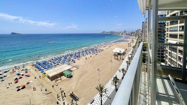 Une plage avec des parasols et des gens, un ciel dégagé et une vue sur la ville en arrière-plan.