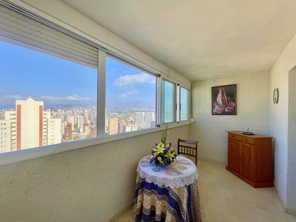 A balcony with a city view, a table with a lace tablecloth, a chair, and a wooden cabinet. - VACANZA HOLIDAY RINCON N092 (Benidorm)