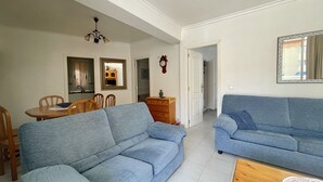 A living room with two blue sofas, a wooden coffee table, and a dining area with a table and chairs.