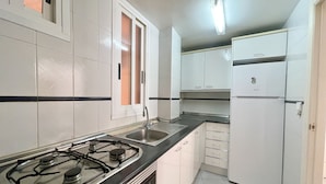 A kitchen with white cabinets, a black countertop, a gas stove, a sink, and a white refrigerator.
