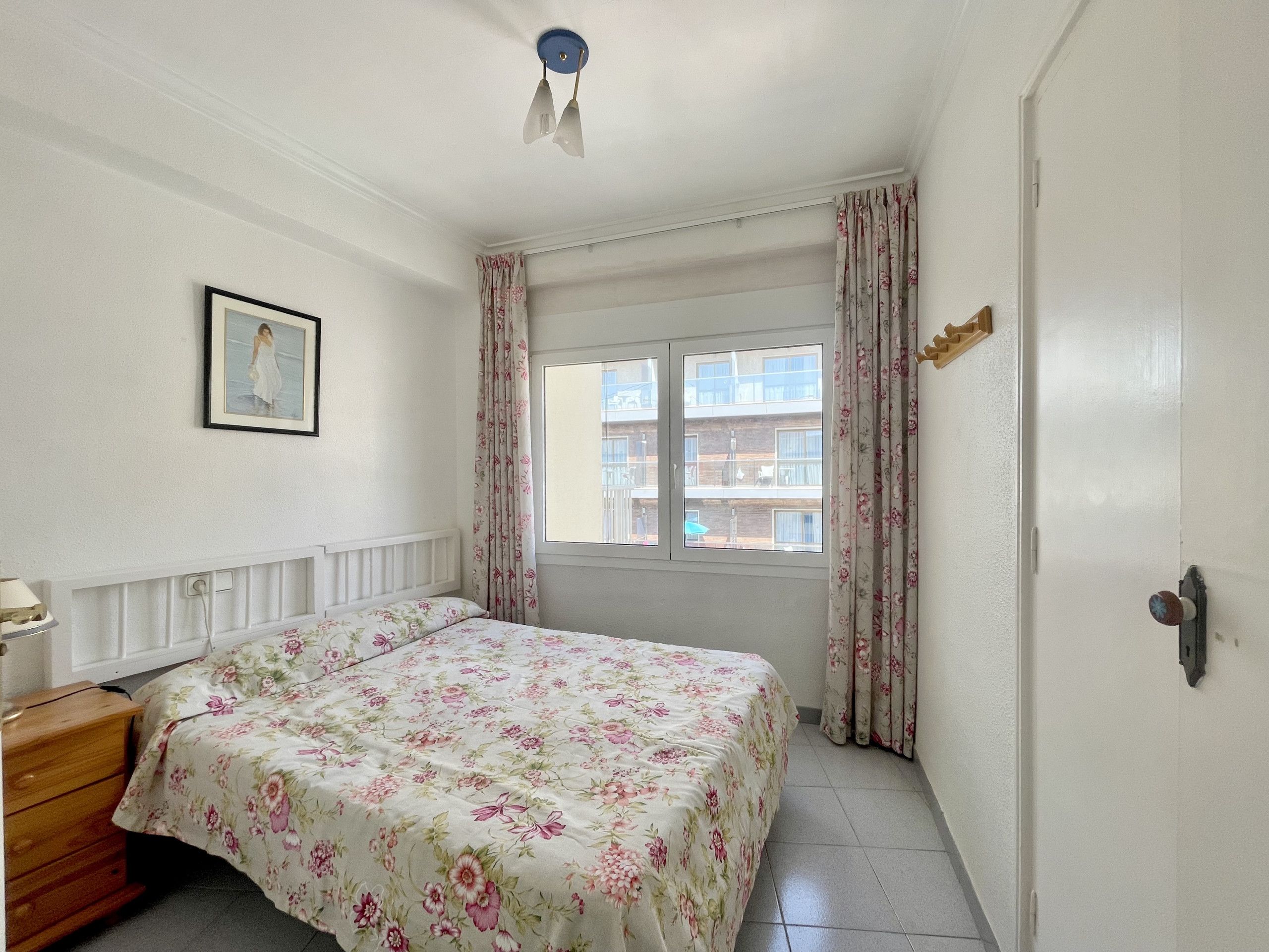 A bedroom with a bed, a dresser, a window with curtains, and a picture on the wall.