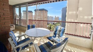 A balcony with a table and chairs, a view of tall buildings, and a brick wall. - PRINCIPADO WIFI, AIRCO, POOL AND GARDEN N031 (Benidorm)