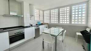 A modern kitchen with white cabinets, a black stove, and a glass dining table with white chairs. - PRINCIPADO WIFI, AIRCO, POOL AND GARDEN N031 (Benidorm)