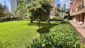 A well-maintained garden with a variety of trees and shrubs, surrounded by high-rise buildings. - PRINCIPADO WIFI, AIRCO, POOL AND GARDEN N031 (Benidorm)