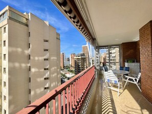 A balcony with a red railing, a table, and chairs, overlooking a cityscape with multiple buildings. - PRINCIPADO WIFI, AIRCO, POOL AND GARDEN N031 (Benidorm)