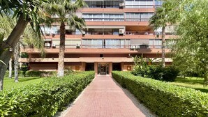 A multi-story building with a central entrance, surrounded by well-maintained hedges and palm trees. - PRINCIPADO WIFI, AIRCO, POOL AND GARDEN N031 (Benidorm)