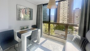 A modern living room with a dining area, large windows, and a view of tall buildings. - PARAISO LEVANTE BEACH STUDIO N105 (Benidorm)