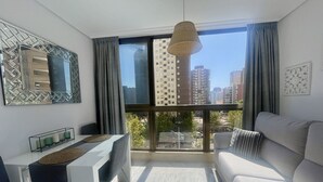 A modern living room with a large window, a white sofa, a desk, and a hanging lamp. - PARAISO LEVANTE BEACH STUDIO N105 (Benidorm)