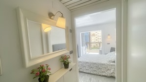 A hotel room with a large mirror, a bedside table with a vase of flowers, a bed with a floral bedspread, and a view of the outside balcony. - PARAISO LEVANTE BEACH STUDIO N105 (Benidorm)