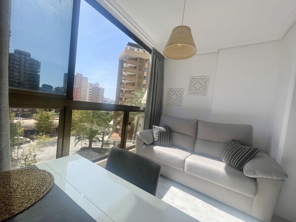 A modern living room with a large window, a sofa, a hanging light fixture, and a dining table. - PARAISO LEVANTE BEACH STUDIO N105 (Benidorm)
