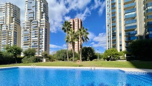Una piscina amb aigua cristal·lina blava, envoltada d'edificis residencials alts i palmeres.