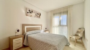 Un dormitori amb un llit, fallegueres, una cadira, una finestra amb cortines i una làmpada al sostre.