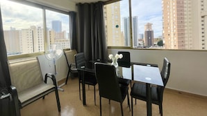 A hotel room with a dining area, large windows, and a view of tall buildings. - NEW TOWN LEVANTE BEACH (N121) (Benidorm)