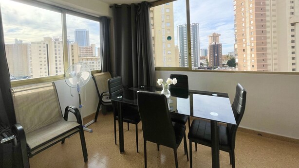 A hotel room with a dining area, large windows, and a view of tall buildings. - NEW TOWN LEVANTE BEACH (N121) (Benidorm)