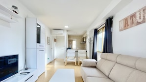 A modern, well-lit living room with a flat-screen TV, a white coffee table, a beige sofa, and a kitchen area in the background. - NEW TOWN LEVANTE BEACH (N121) (Benidorm)